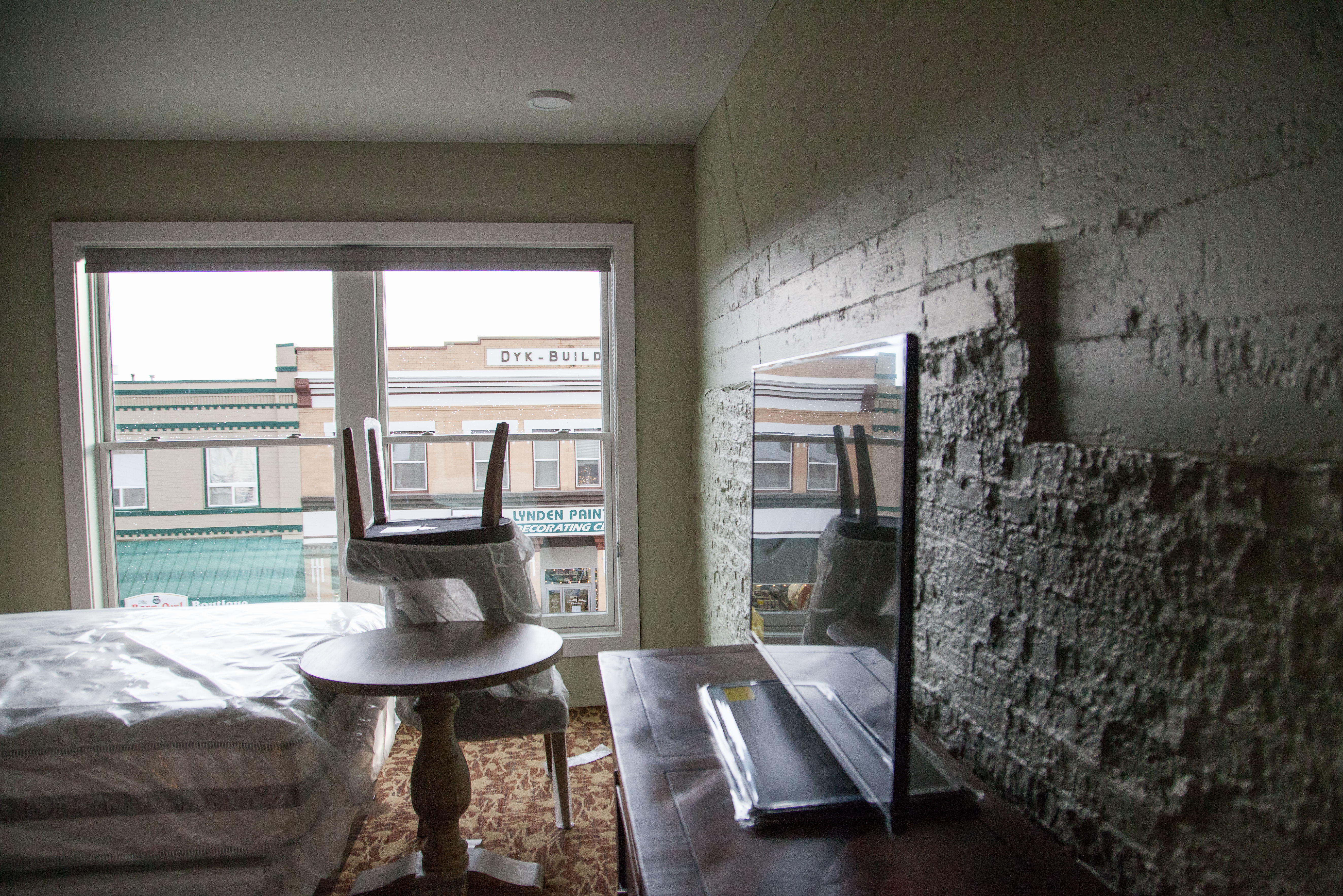 Another Town Room overlooking Front Street, with historic exposed brick behind a modern LG flat TV, and still-wrapped furniture.