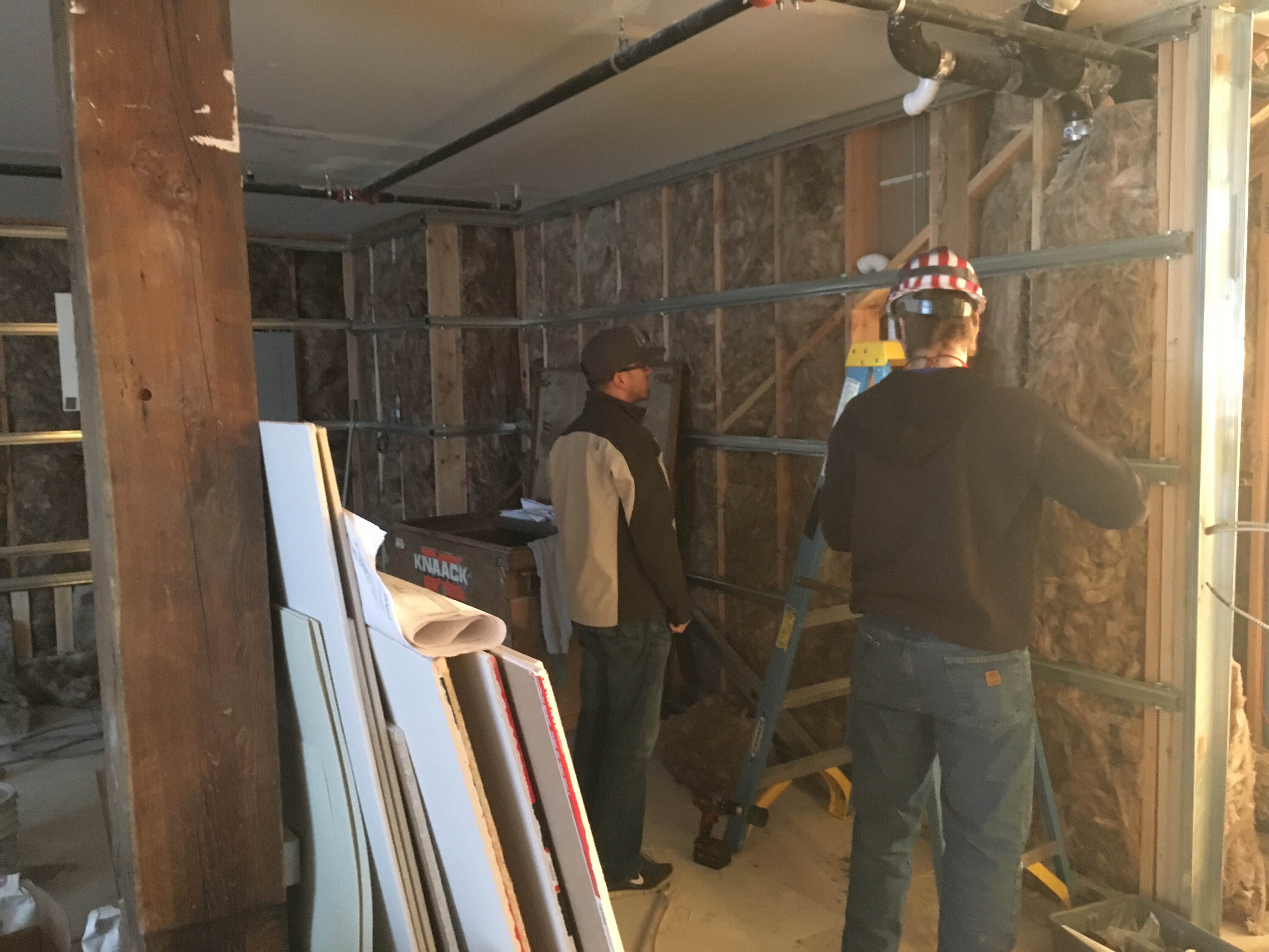 Overflow Taps partner Jesse Nelson looks on as a contractor (also named Jesse) prepares plumbing through a wall to what will be the bar and tap area.